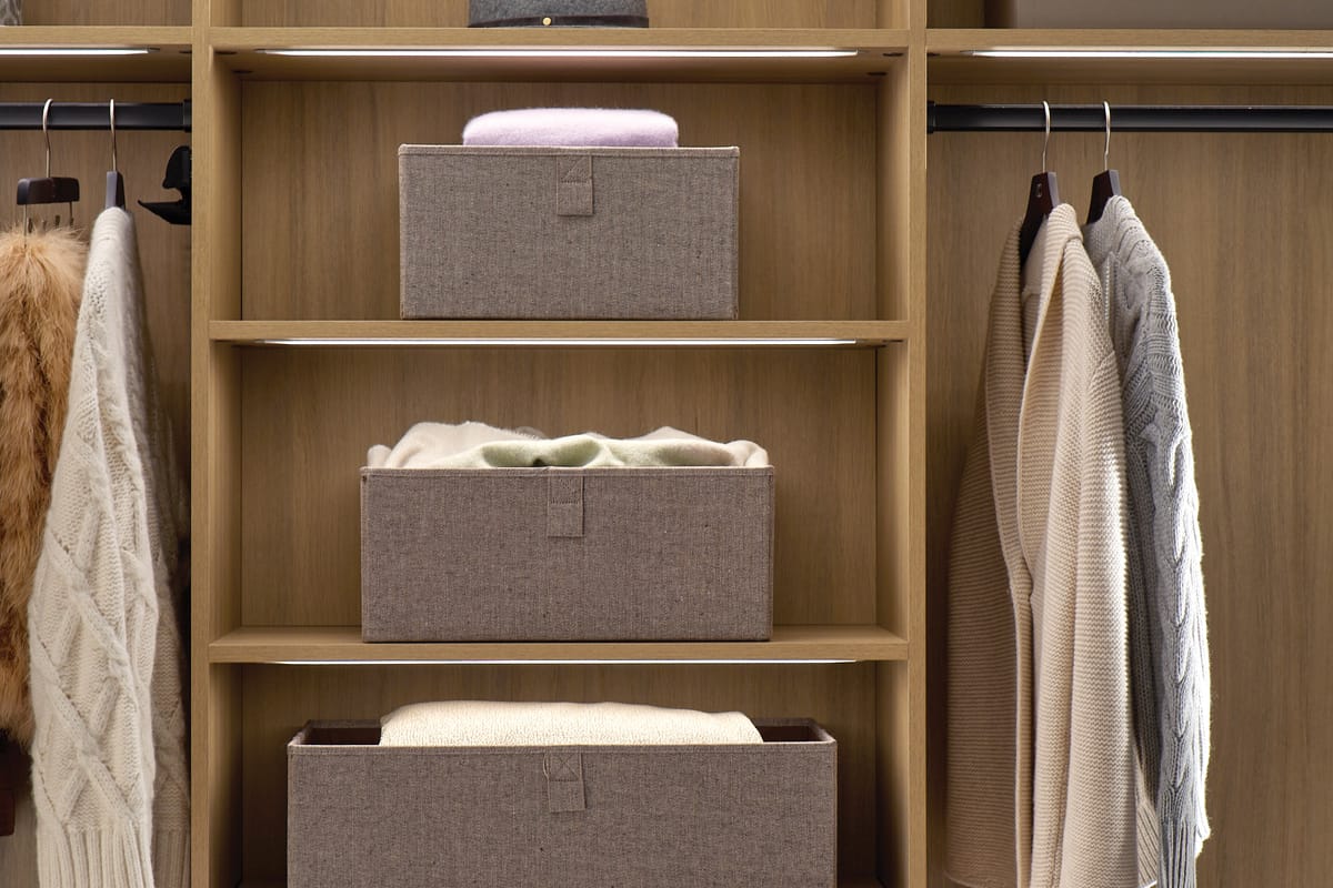 Closet with open shelving and LED lighted clothes rods in natural wood grain finish by California Closets
